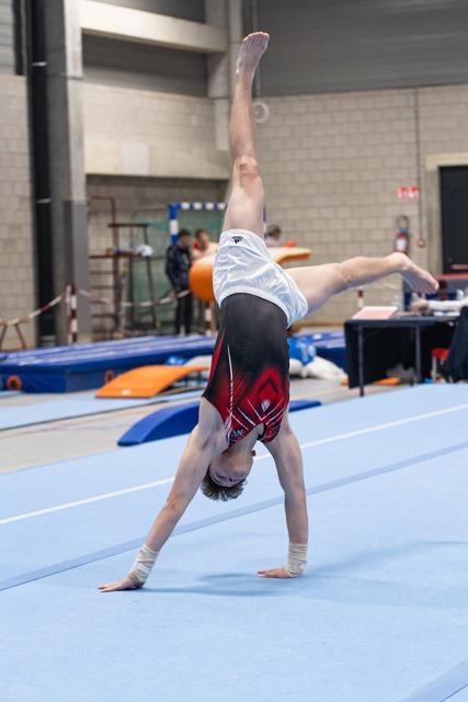 Gymnast in burgundy and white uniform executes a one-handed cartwheel on blue floor mat in training facility