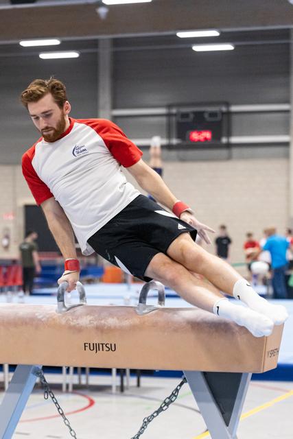 Male gymnast executing pommel horse routine with focused concentration in indoor training facility