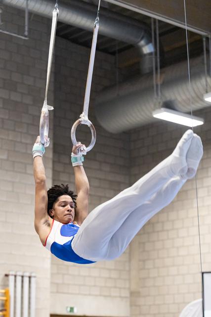Gymnast executes a horizontal hold on still rings, legs extended, showing strength and control in an indoor training facility