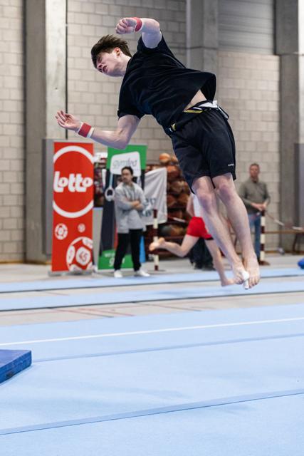 Male gymnast executes a powerful jump on blue floor mat, arms and legs extended mid-air during floor exercise routine