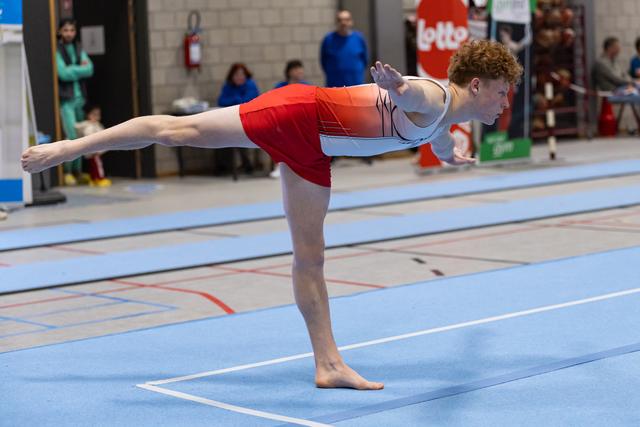 Young gymnast holds an arabesque position on floor mat, extending leg and arms with focused concentration during routine
