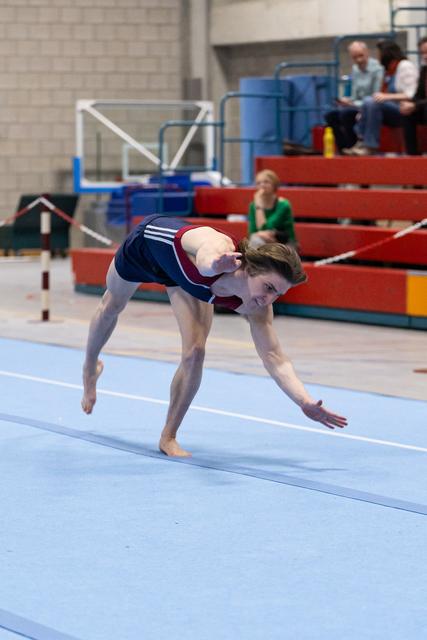 Gymnast performs a backward bend during floor routine, demonstrating flexibility in a training facility