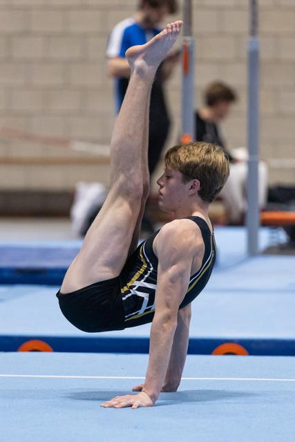 Male gymnast performs a press handstand on floor exercise, demonstrating strength and balance in black competition leotard