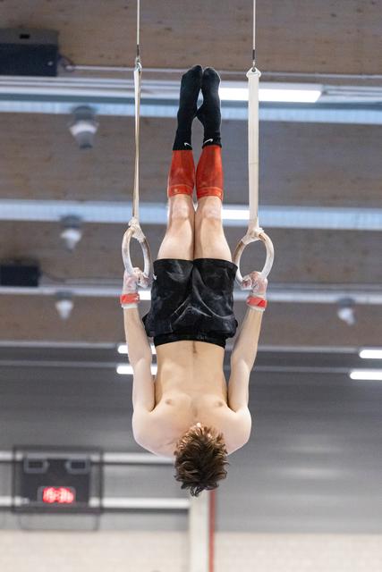 Gymnast hanging upside down on rings in inverted position, arms extended, demonstrating strength and control