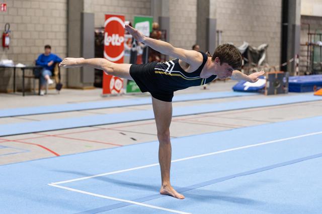 Male gymnast performs elegant scale balance on floor mat, body parallel to ground with arms and leg extended during routine