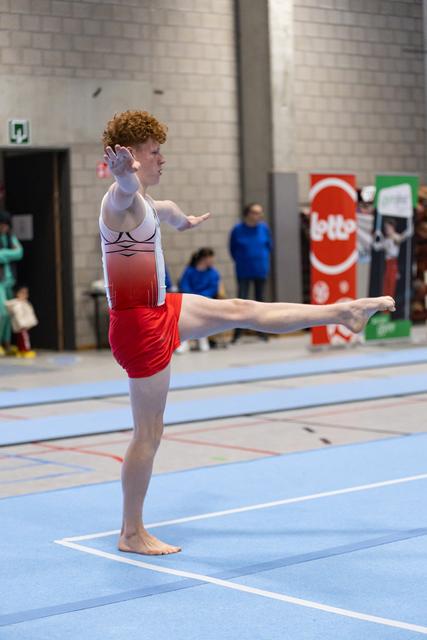 Male gymnast performs floor routine with high leg extension and expressive arm gestures in indoor training facility