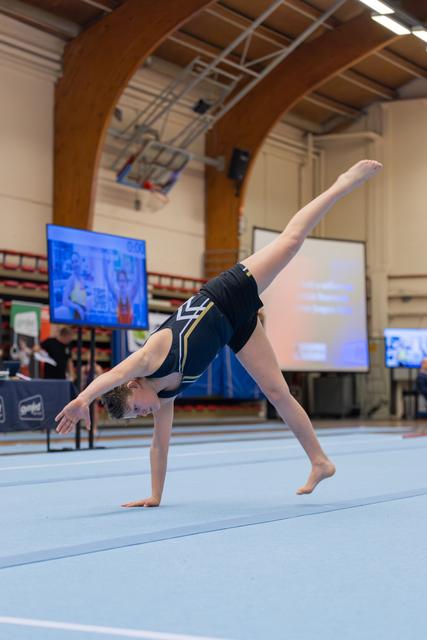 Young gymnast performing a one-handed cartwheel on the floor, leg extended high, focused and controlled during competition.