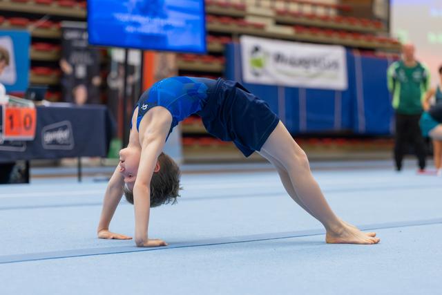 Young gymnast performs a back bridge position on the floor mat during a gymnastics meet, head inverted, focused.