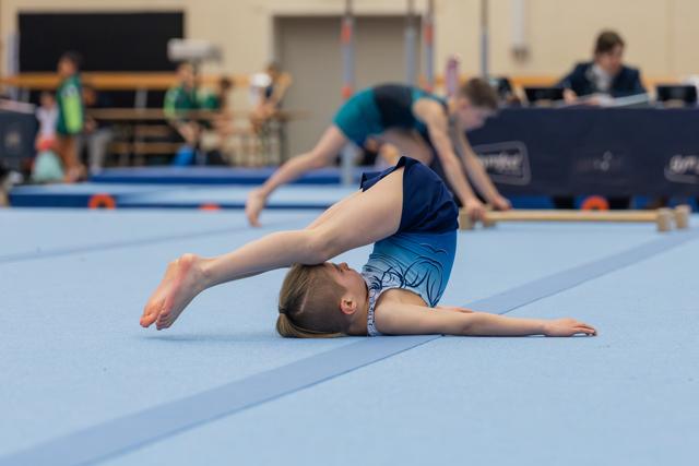 Young gymnast performs a backbend on the floor exercise mat, feet overhead, focused during a gymnastics meet.