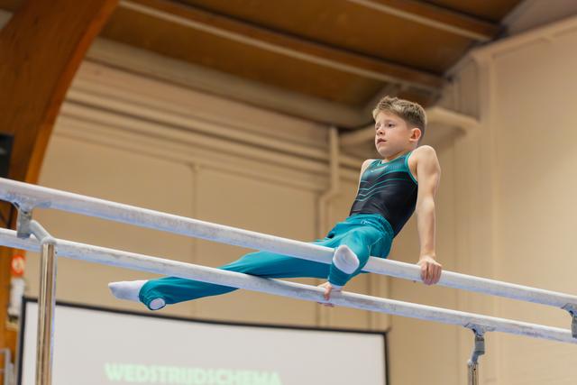 Focused young boy performing on parallel bars, balancing with concentration in a gymnastics hall.