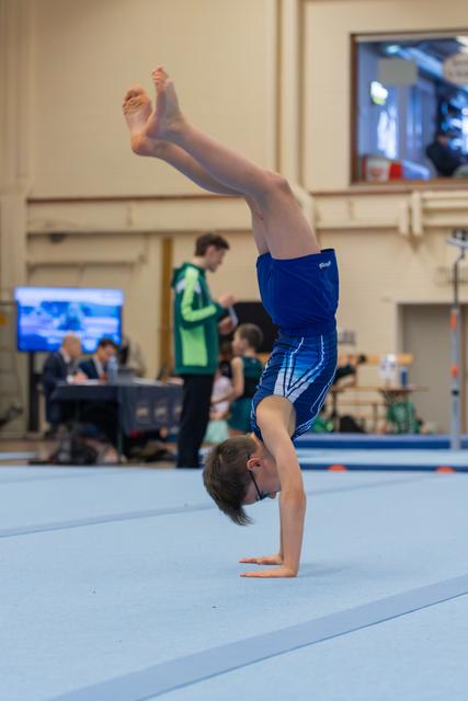 Boy in blue shorts performing a handstand on the floor exercise mat during a gymnastics competition.