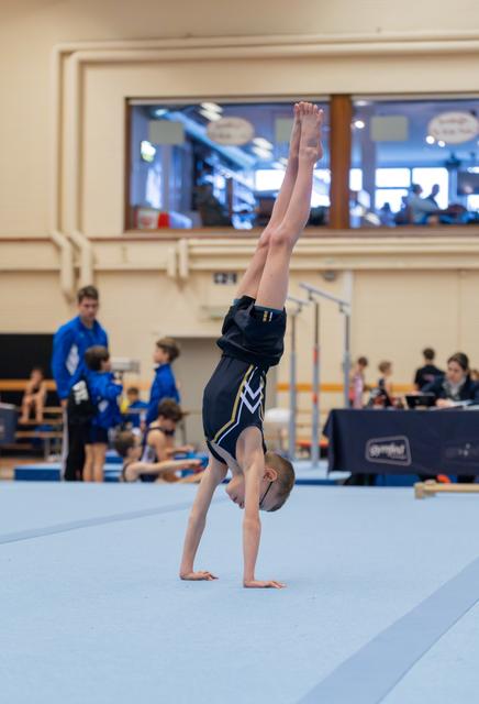 Young boy performing a perfect handstand on the floor exercise mat during a gymnastics competition, legs straight overhead.
