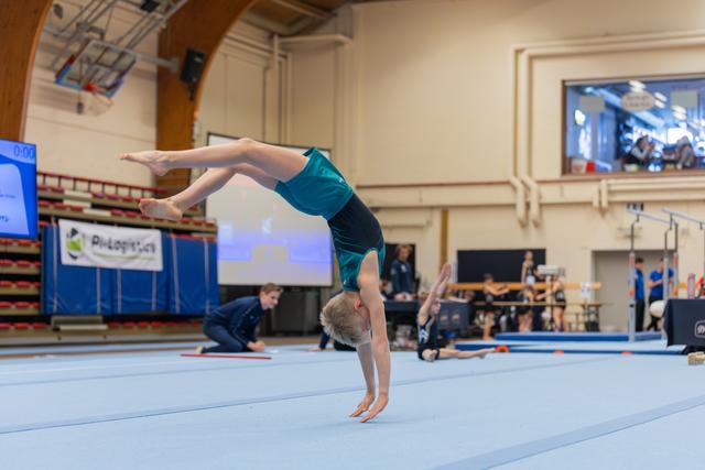 Young gymnast performs a handstand on the floor exercise mat, body arched with legs extended, in a gymnastics hall.