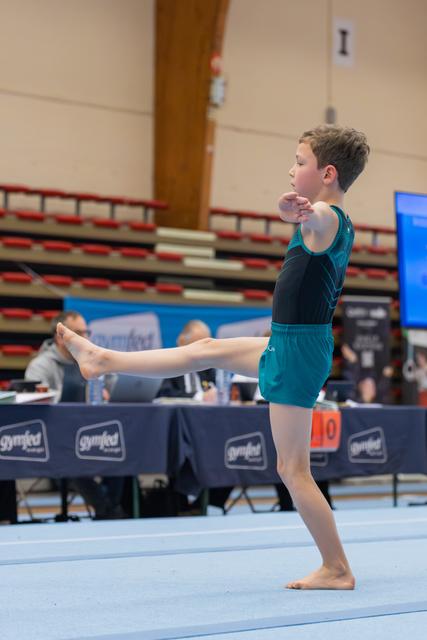 Young boy gymnast performing a precise leg raise on the floor, focused and composed during a gymnastics meet.