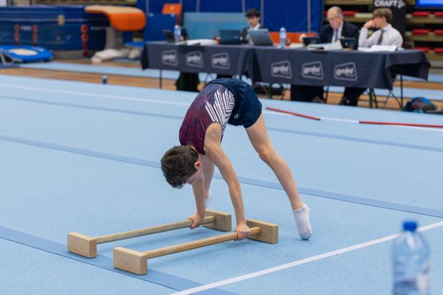 Young male gymnast bent over parallel floor bars, concentrating intensely during a gymnastics meet on blue matting.