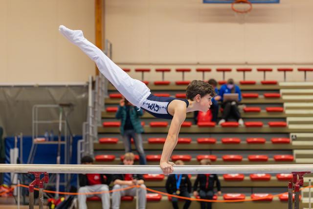 Young male gymnast executes a precise horizontal hold on parallel bars, body perfectly parallel to the ground in a competitive gym.