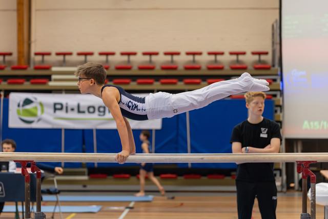 Young gymnast holds a perfect horizontal planche on parallel bars, body fully extended, focused expression, indoor gym.
