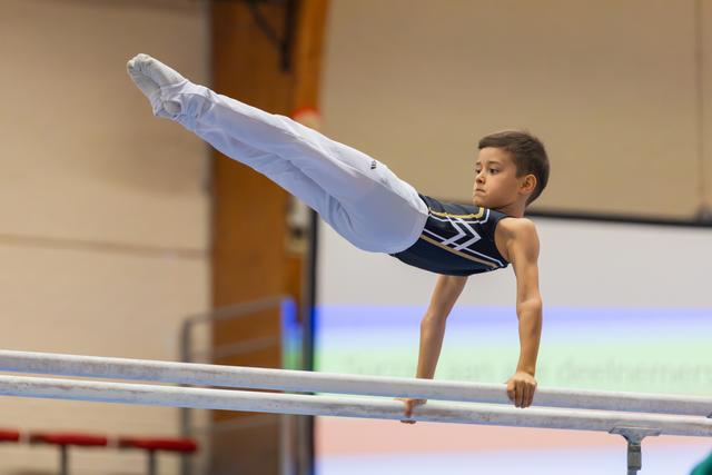 Focused young male gymnast performs a powerful L-sit hold on parallel bars, legs extended parallel to the floor.
