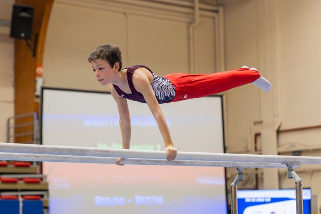 Young male gymnast holds a planche on parallel bars, body horizontal, expression focused and determined during a gymnastics meet.