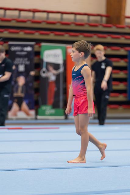 Young male gymnast walks barefoot across the blue floor mat, composed and focused before his routine.
