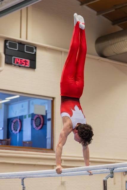 Canadian gymnast performs a perfect handstand on parallel bars, body fully extended and legs pointing upward.