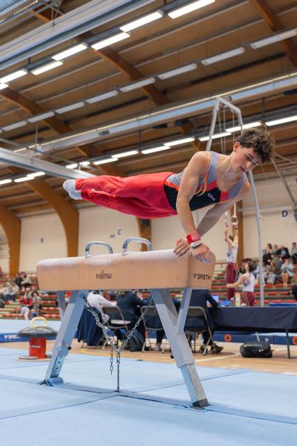 Young male gymnast performs a determined horizontal hold on the pommel horse during an indoor competition.