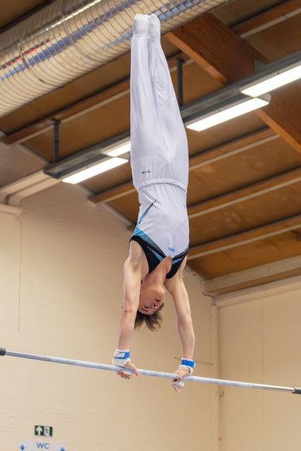 Young male gymnast holds a perfect handstand on the high bar, body fully extended, in an indoor gymnasium.
