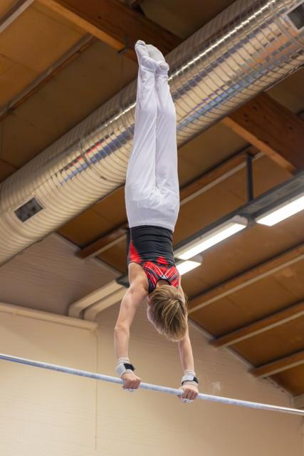 Young male gymnast holds a perfect handstand on the high bar, body fully extended, in an indoor gymnasium.
