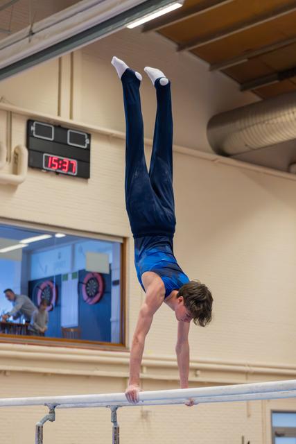 Young male gymnast holds a perfect handstand on parallel bars, legs straight up, in an indoor gymnasium.