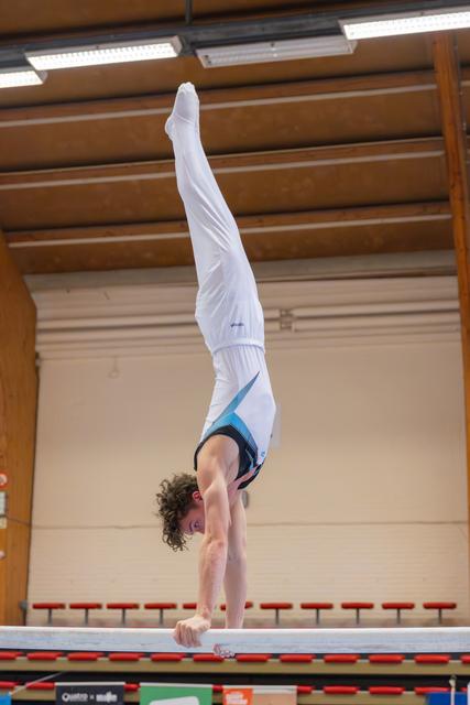 Young male gymnast performs a perfect handstand on parallel bars, body fully extended, in an indoor gymnasium.