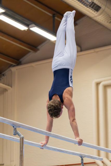 Young male gymnast holds a perfect handstand on parallel bars, body fully extended, legs vertical in a gymnasium.
