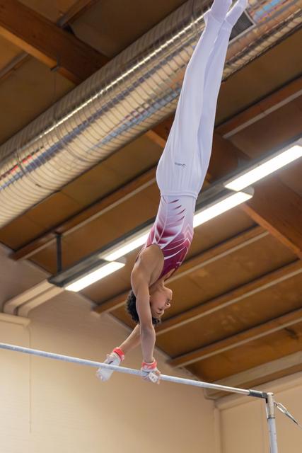 Young gymnast holds an inverted handstand on the uneven bars, legs extended skyward, in an indoor gymnasium.