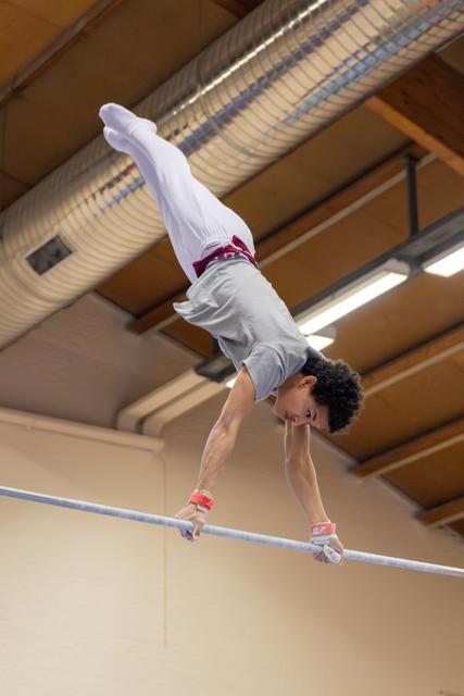 Young male gymnast holds a precise handstand on the high bar, body fully extended, intense concentration in an indoor gym.
