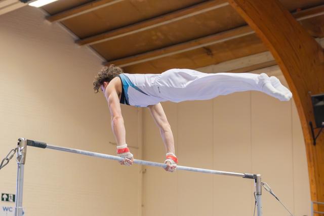 Male gymnast performs a planche on the horizontal bar, body horizontal, showing remarkable strength and control indoors.