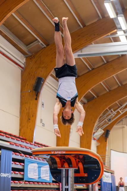 Young male gymnast performs a handstand above a Spieth vault, body fully extended, in an indoor gymnastics arena.