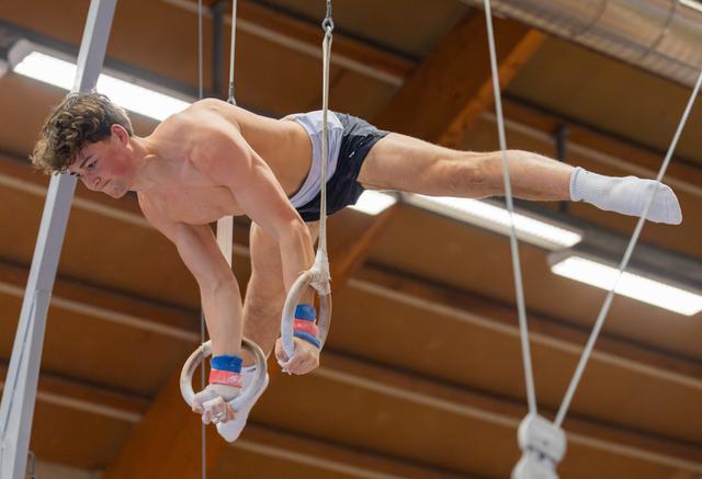 Young male gymnast executing an iron cross on still rings, body perfectly horizontal, expression intense with concentration.