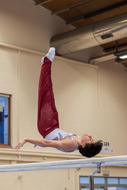 Young gymnast performs a dramatic back arch release on parallel bars, legs extended upward, expression focused and intense.