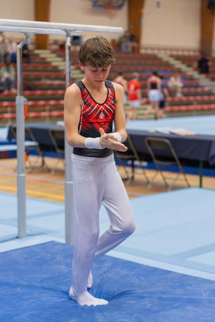 Young male gymnast carefully applies chalk to his hands before his parallel bars routine, focused and composed.