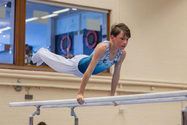 Focused young male gymnast performs a horizontal hold on parallel bars, body parallel to floor, in an indoor gymnasium.