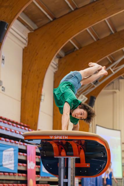 Young gymnast performs a handspring vault on a Spieth apparatus, body fully inverted mid-flight in an indoor sports hall.