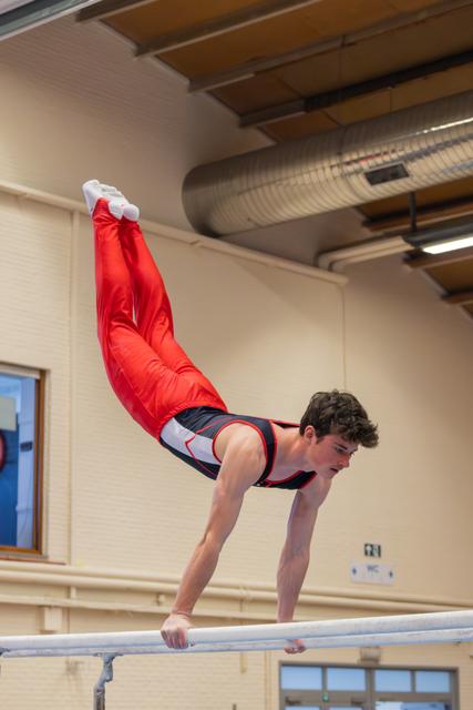 Young male gymnast performs a dramatic horizontal hold on parallel bars, body parallel to the floor, legs raised high.