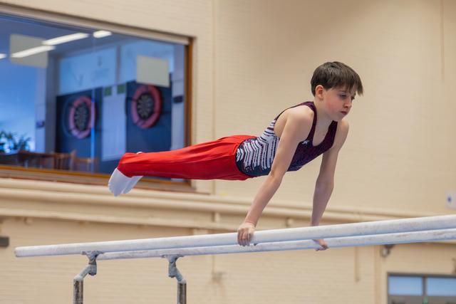 Focused boy performing a planche hold on parallel bars, body perfectly horizontal, showing strength and concentration.