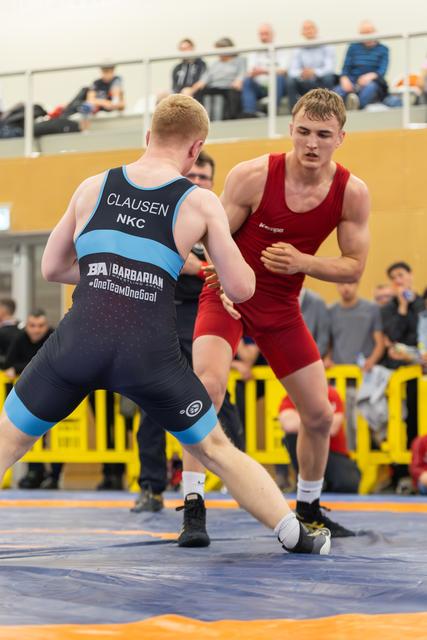 Clausen (NKC) in black singlet squares off against a red-clad opponent, both in tense athletic stances on the mat.