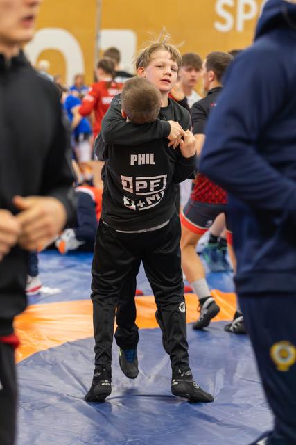 Young wrestler Phil lifts his opponent off the mat, both showing intense focus during a youth wrestling bout.