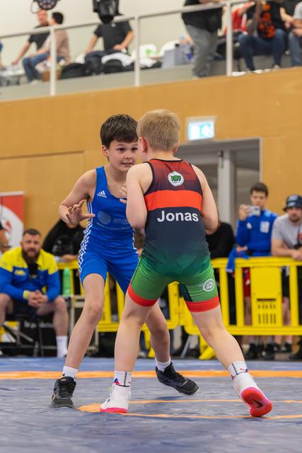 Two young boys face off on the mat, the boy in blue bracing confidently against Jonas in a dark singlet.