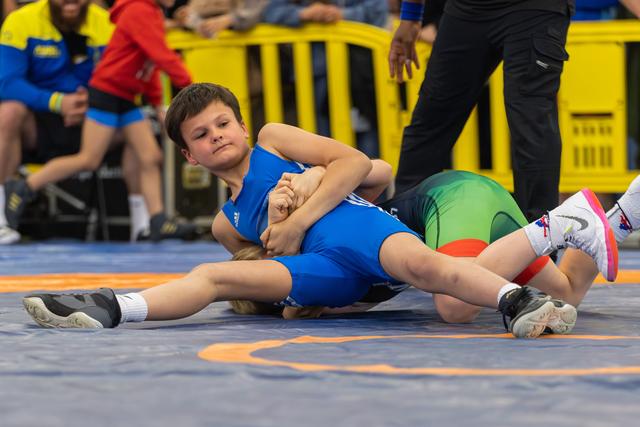 Focused young wrestler in blue singlet pins his opponent on the mat during a youth wrestling match.