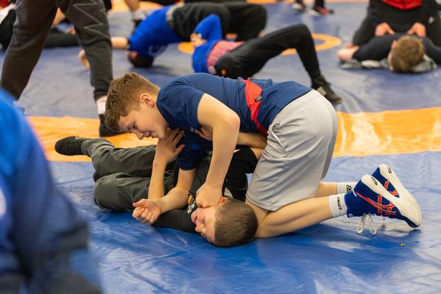 Determined boy in blue singlet pins opponent to the mat during a youth wrestling practice session.