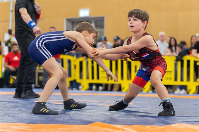 Two young wrestlers grip each other's wrists in a tense standoff on the mat, focused and determined.