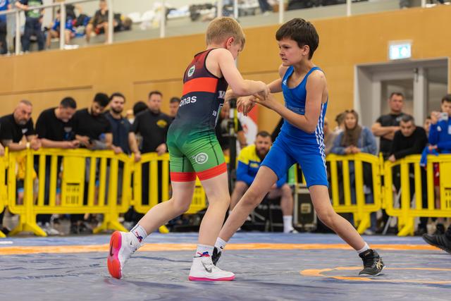 Two young boys face off on the wrestling mat, both in athletic stance, focused and determined during their bout.
