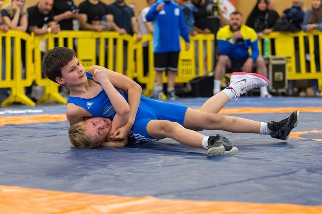 Two young wrestlers in blue singlets, one pinning the other on the mat during an intense youth bout.